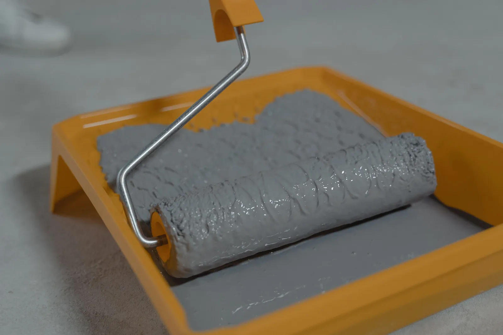 Roller loaded with gray coating in a paint tray